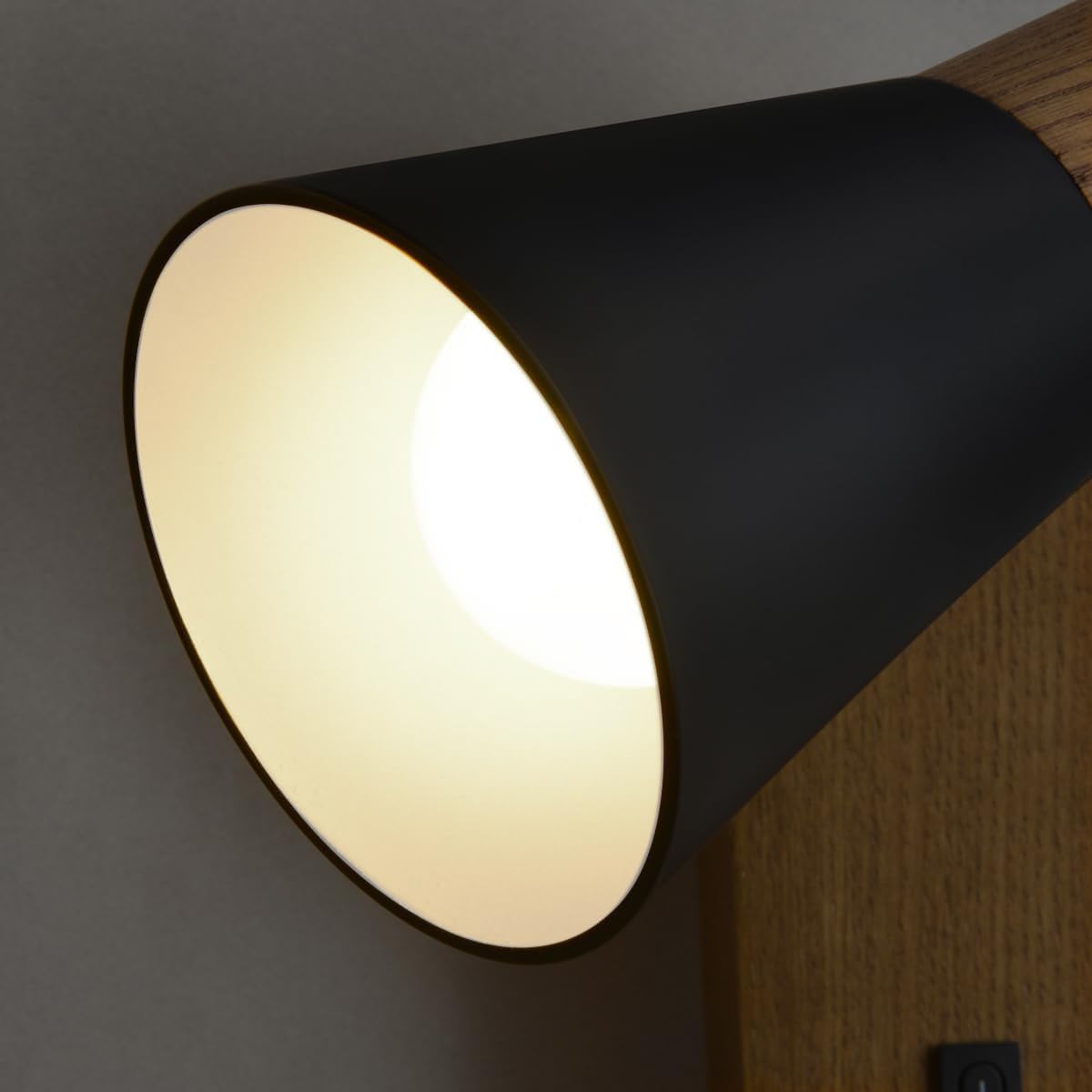 Black wall-mounted light fixture on a gray wall with wooden paneling.