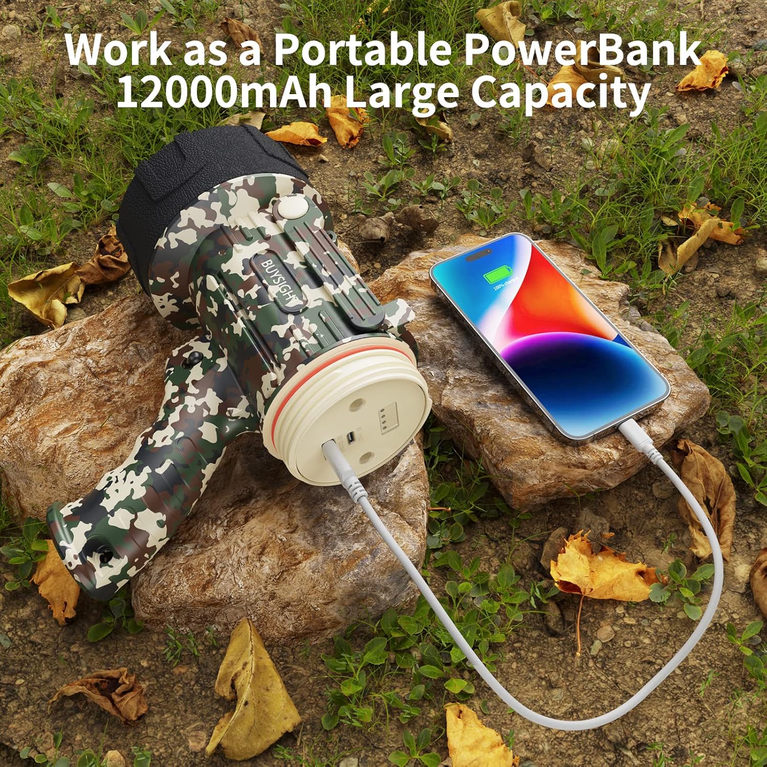 Camouflage portable power bank charging a smartphone outdoors on rocks with leaves.