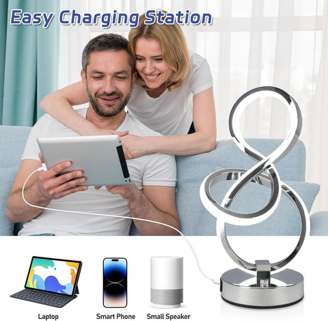 Charging station with cable connected to laptop, phone, and speaker, with a couple using a tablet in the background.