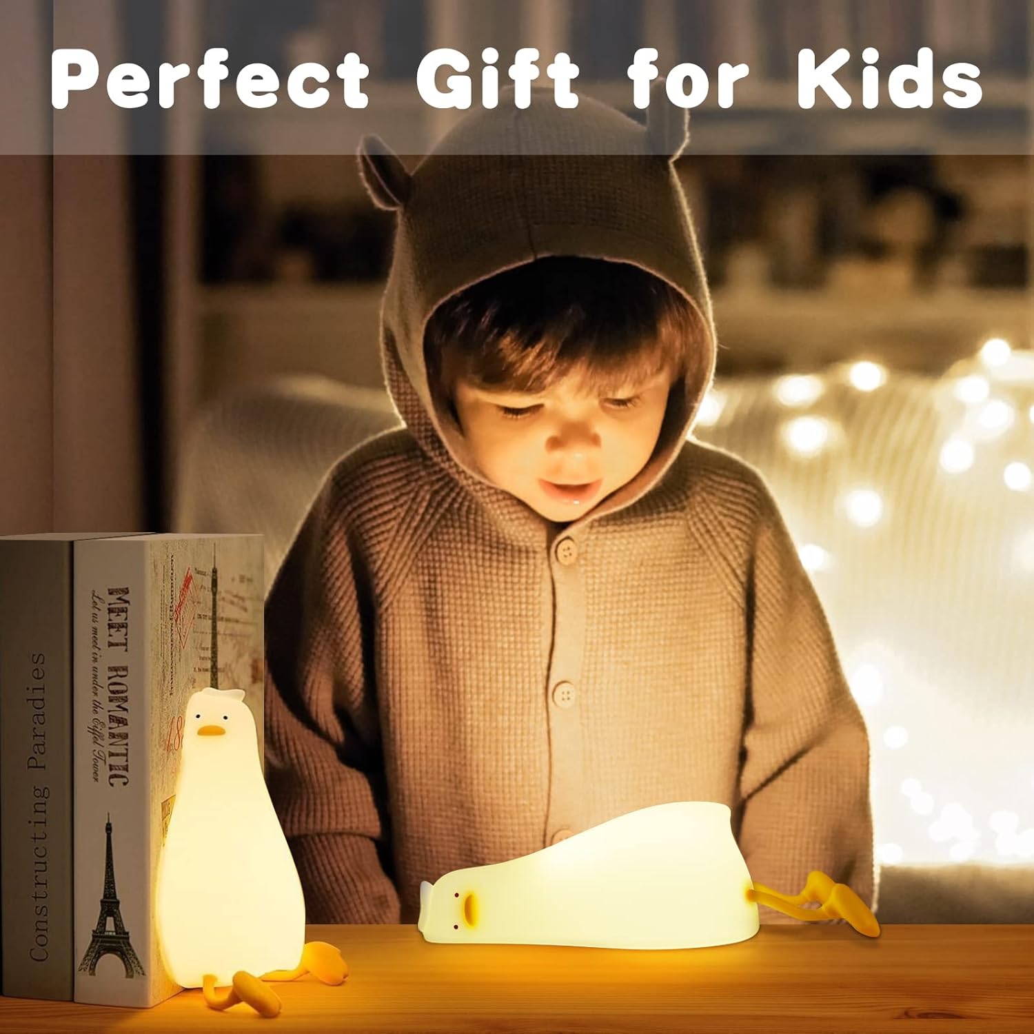 Child in a brown hoodie with animal ears, sitting at a table with a penguin-shaped lamp and book.