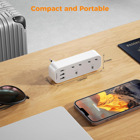 Compact travel adapter on a wooden surface with smartphone, sunglasses, and passport
