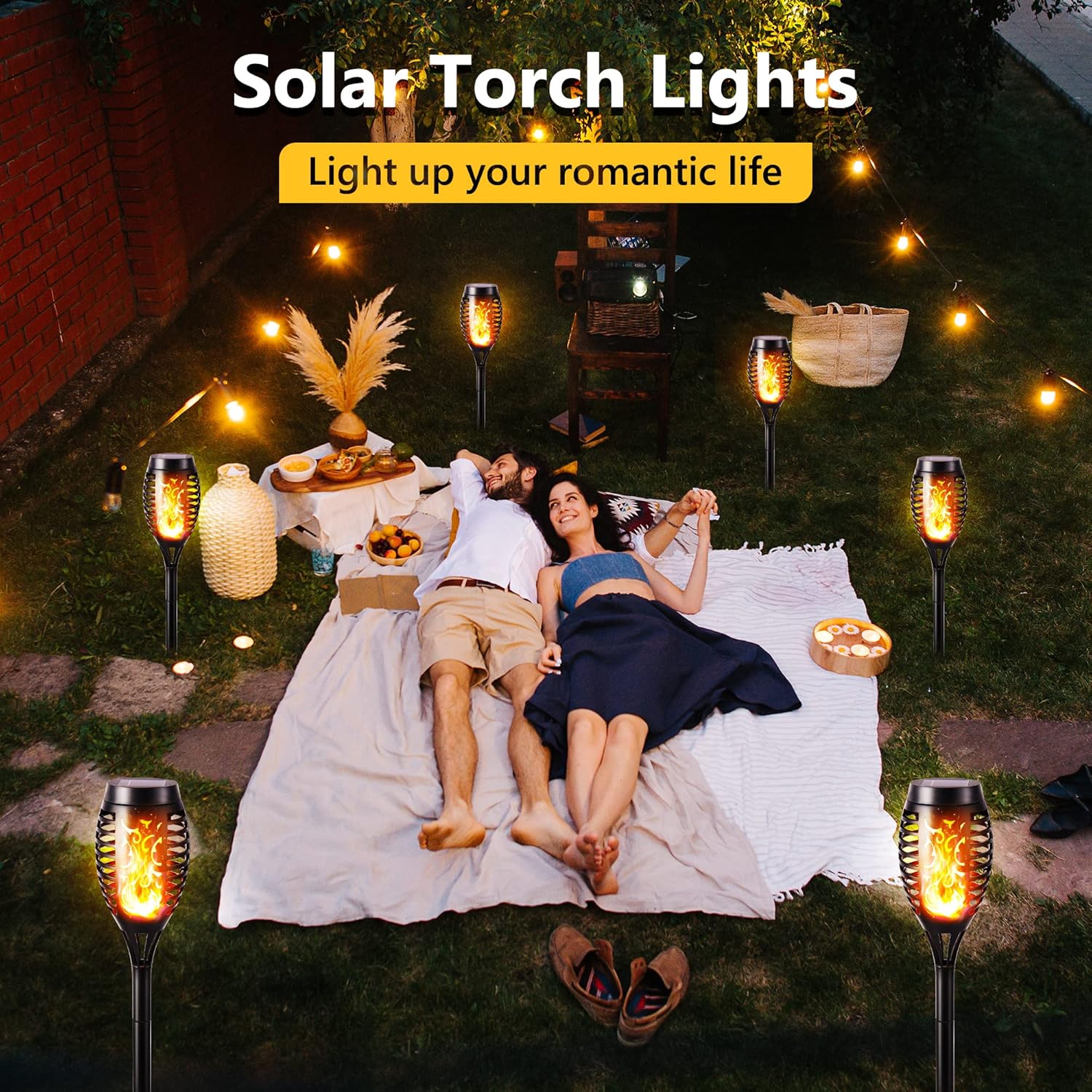 Couple enjoying a romantic picnic with solar torch lights in a garden setting.