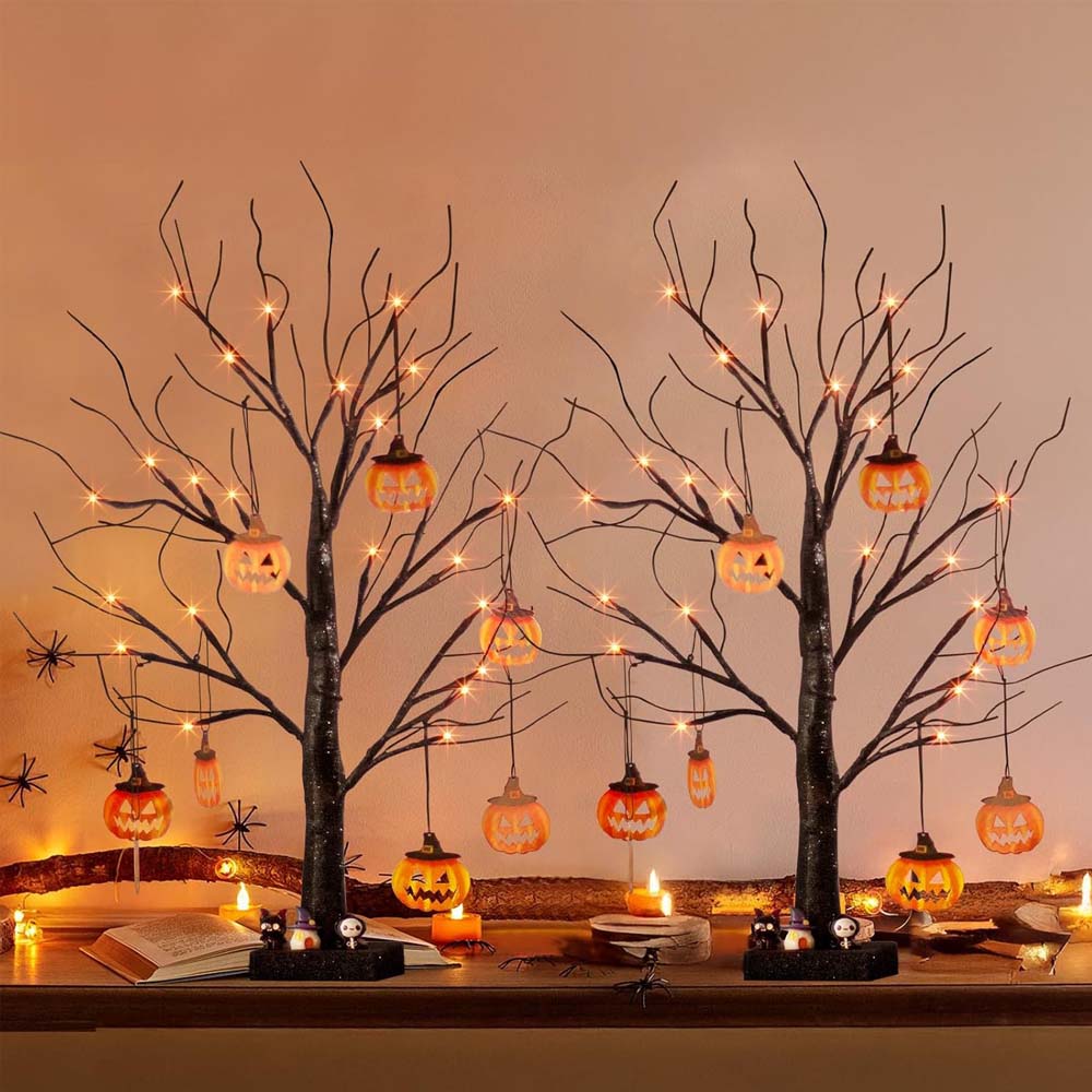 Decorative Halloween setup with bare trees, lit pumpkins, and candles on a table.