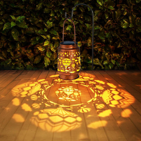 Decorative lantern casting patterns on a wooden floor with green foliage in the background