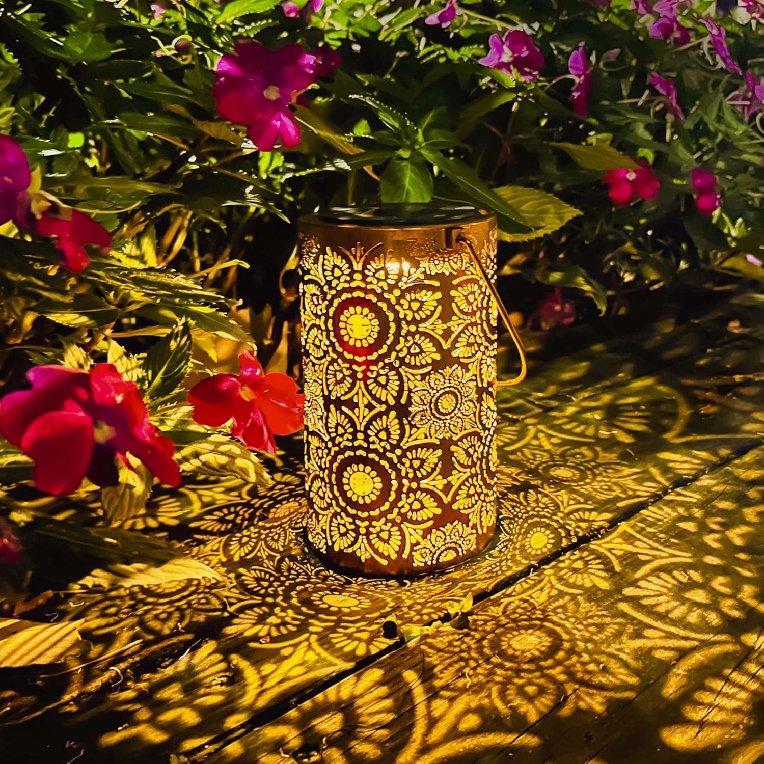 Decorative lantern casting patterns on a wooden surface with flowers in the background