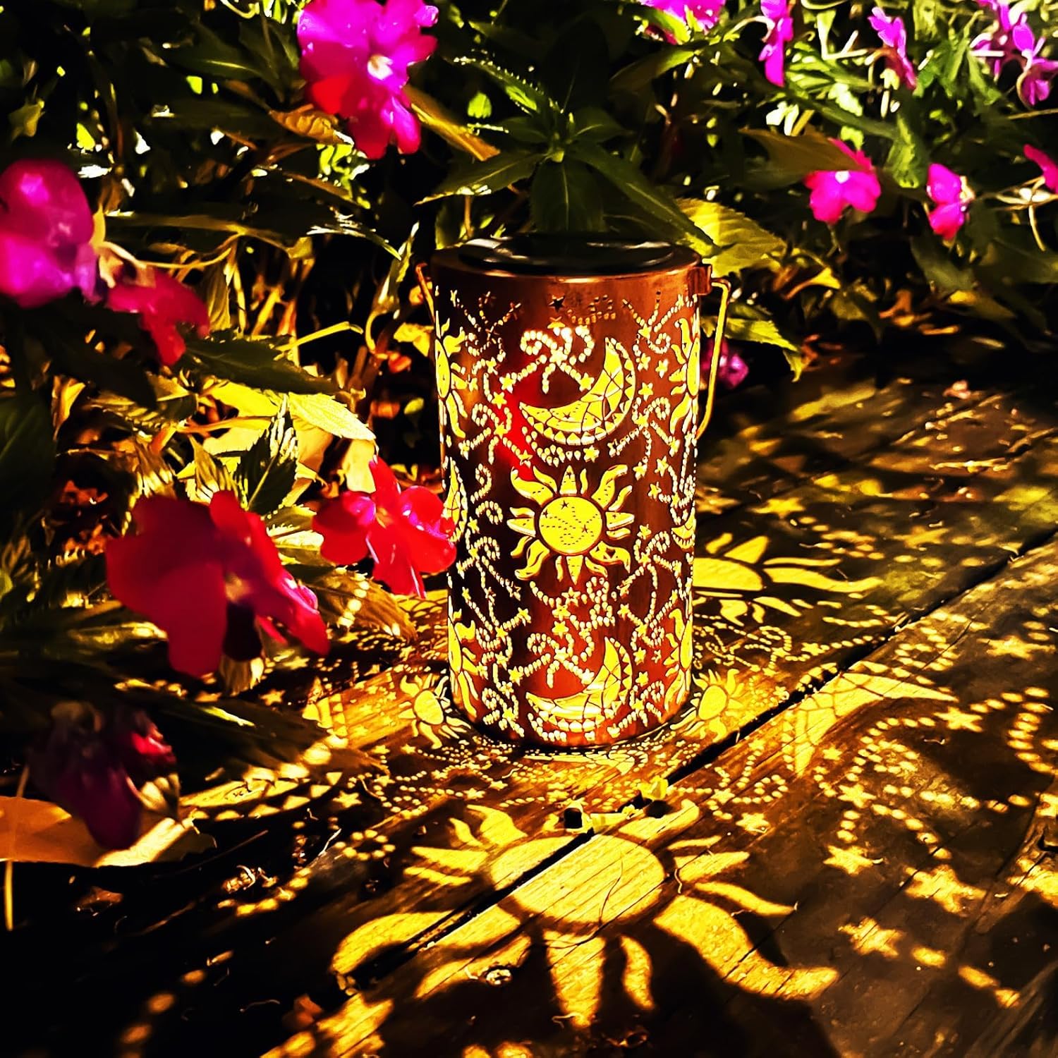 Decorative lantern with sun and moon design casting shadows on a wooden surface with flowers in the background