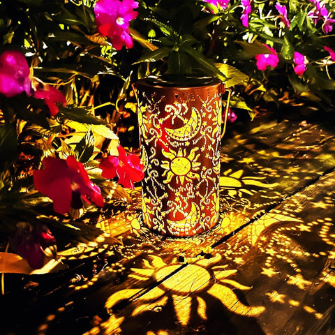 Decorative lantern with sun and moon design casting shadows on a wooden surface with flowers in the background