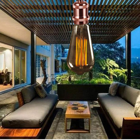 Decorative light bulb hanging above a patio with outdoor furniture and garden view.