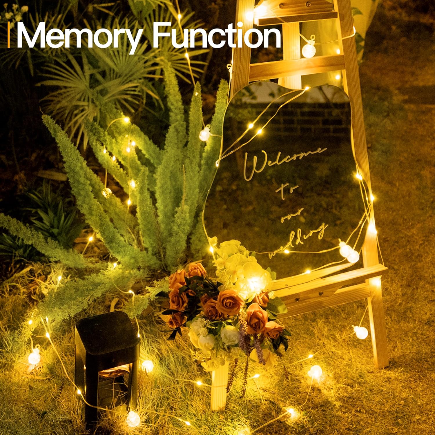 Decorative setup with a mirror, plants, and flowers illuminated by string lights at night.