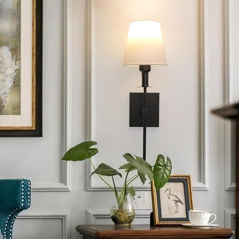 Decorative wall lamp with a plant and framed picture on a table against a paneled wall.