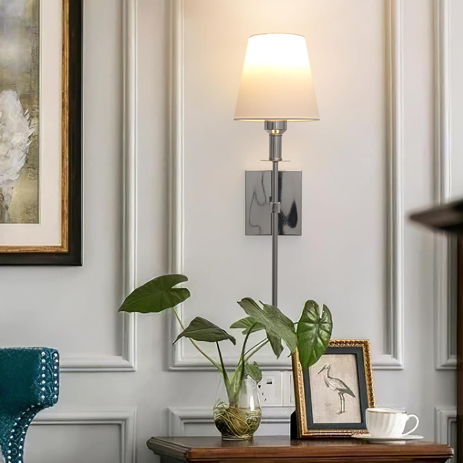 Decorative wall lamp with a plant and framed picture on a wooden surface.