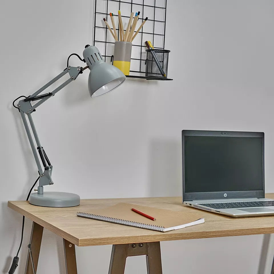 Lamp clamped to a wooden table, illuminating a workspace.​


