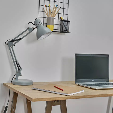 Lamp clamped to a wooden table, illuminating a workspace.​

