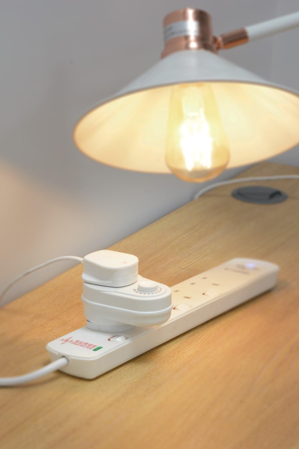Desk lamp on a wooden surface with a power strip and adapter.