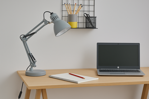 Desk setup with a laptop, notebook, pen, and adjustable lamp on a light wooden desk.