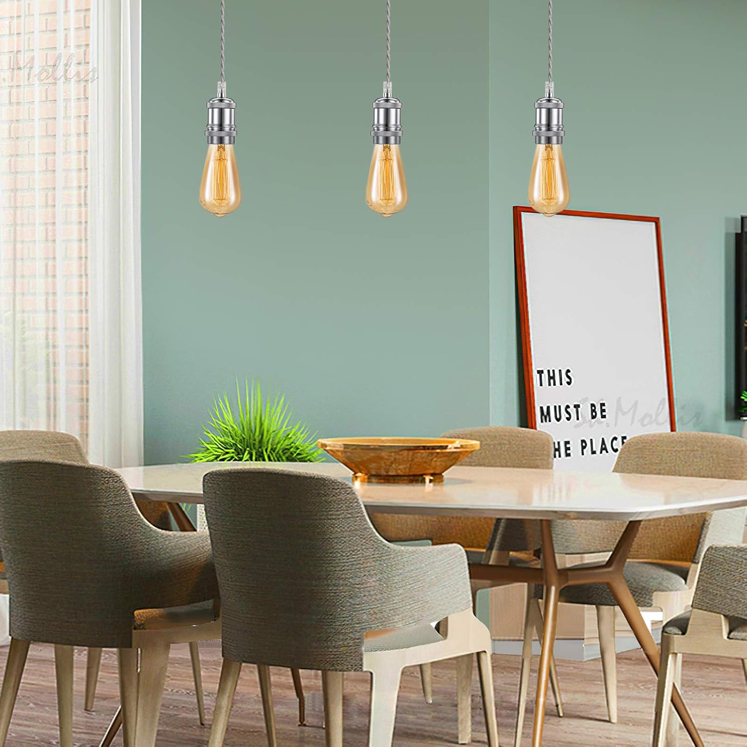 Dining room with round table, chairs, and pendant lights against a green wall.