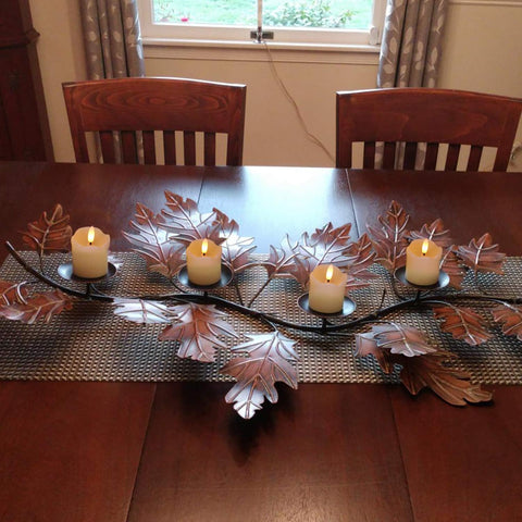 Dining table with leaf-patterned candle holder and candles on a metallic runner.