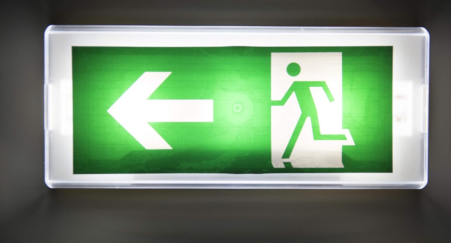 Emergency exit sign with green background and white arrow and person icon on a dark background