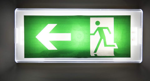 Emergency exit sign with green background and white arrow and person icon on a dark background