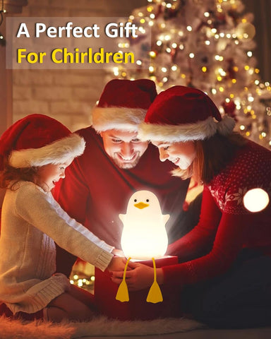 Family with children wearing Santa hats, looking at a glowing penguin-shaped night light in front of a Christmas tree.