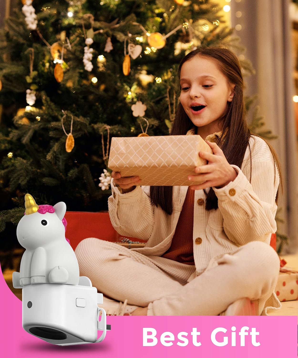 Girl opening a gift with a unicorn-shaped toy in front of a decorated Christmas tree.