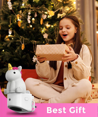 Girl opening a gift with a unicorn-shaped toy in front of a decorated Christmas tree.