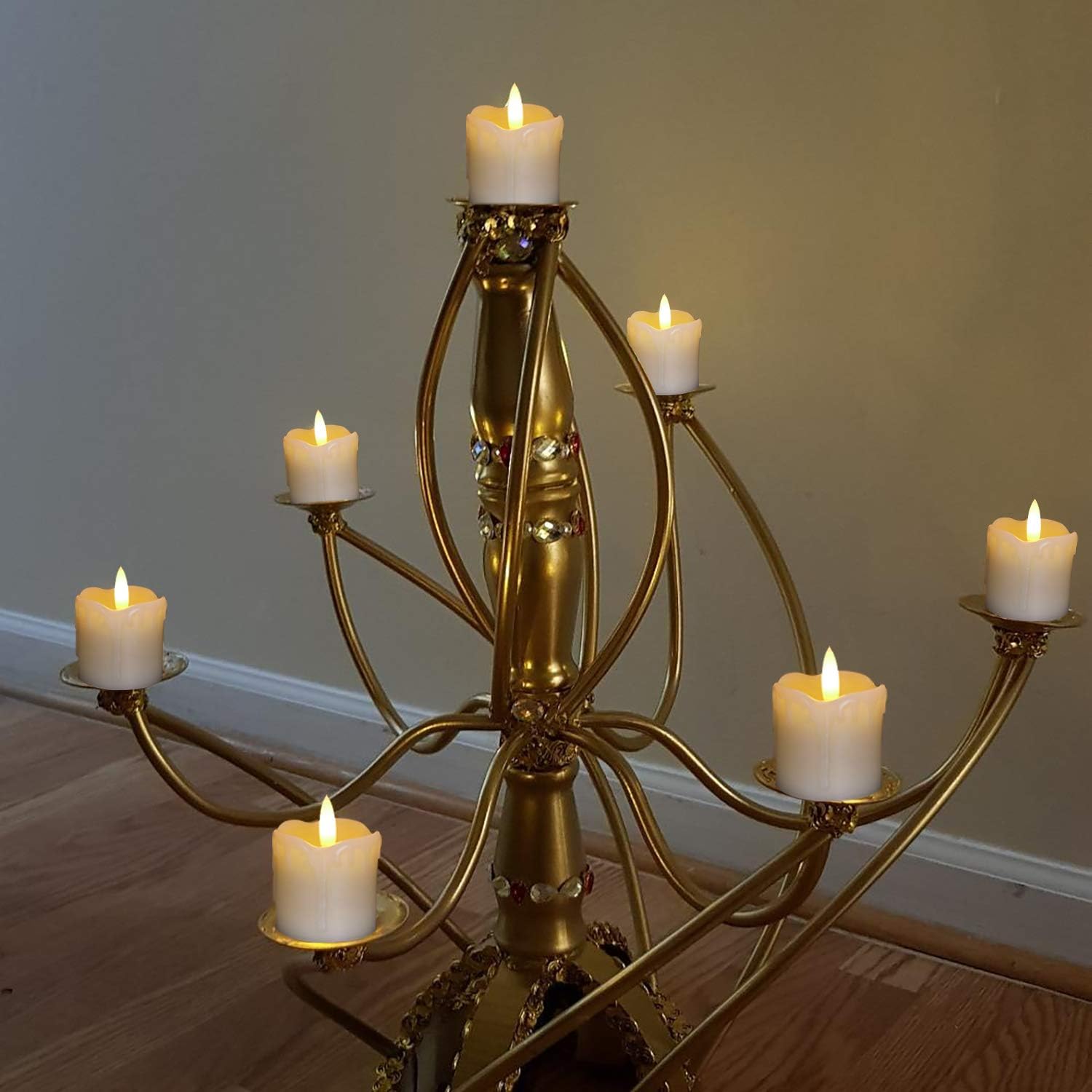 Gold candelabra with six candles on a wooden floor against a plain wall.