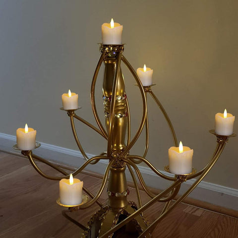 Gold candelabra with six candles on a wooden floor against a plain wall.