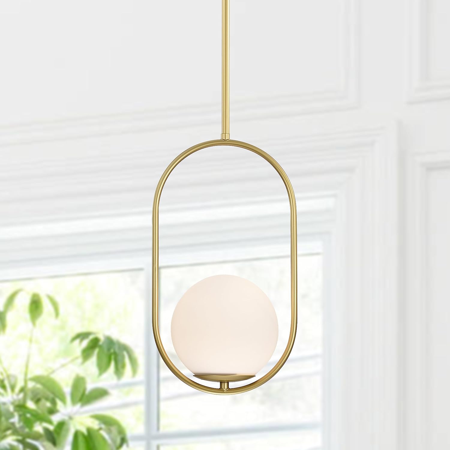 Gold pendant light with a white glass shade in front of a window with blinds.