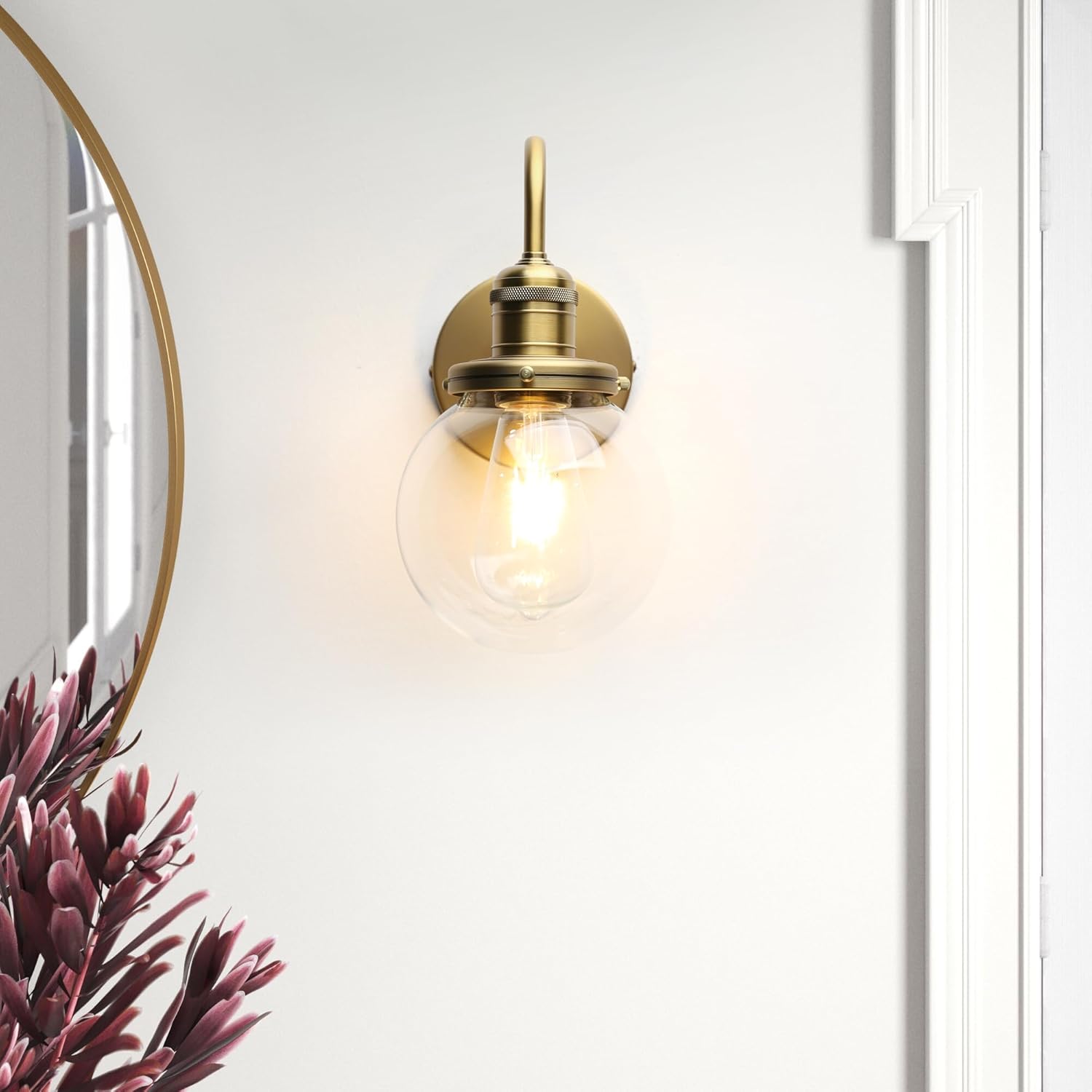 Gold wall-mounted light fixture on a white wall with a plant in the corner.