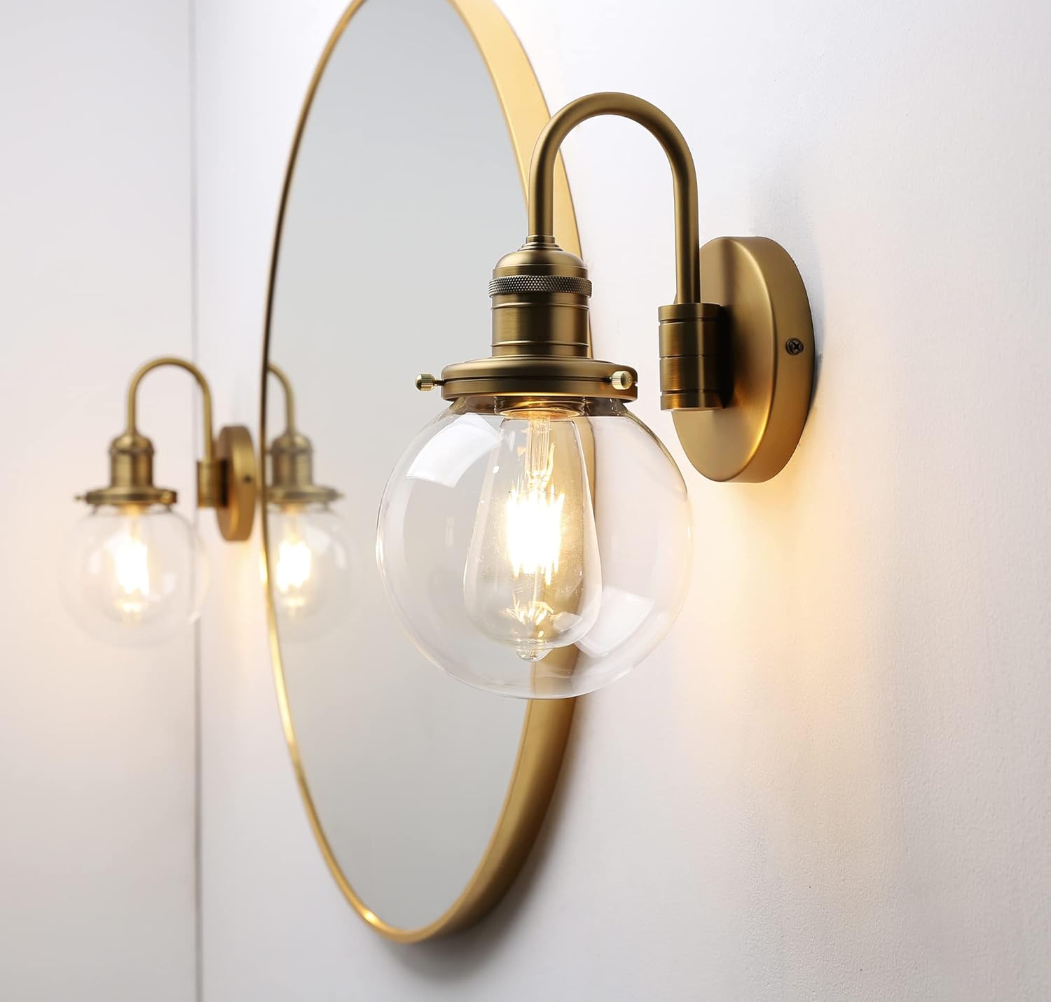 Gold wall sconce with clear glass bulb on a white wall