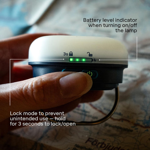 Hand holding a small electronic device with battery level indicator and lock mode feature on a map background.
