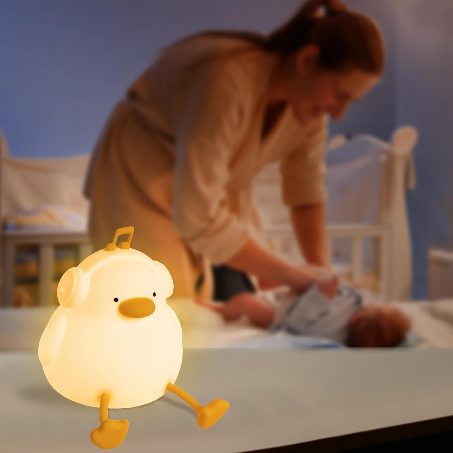 Lamp shaped like a cartoon chick on a table with a blurred background of a person and baby.