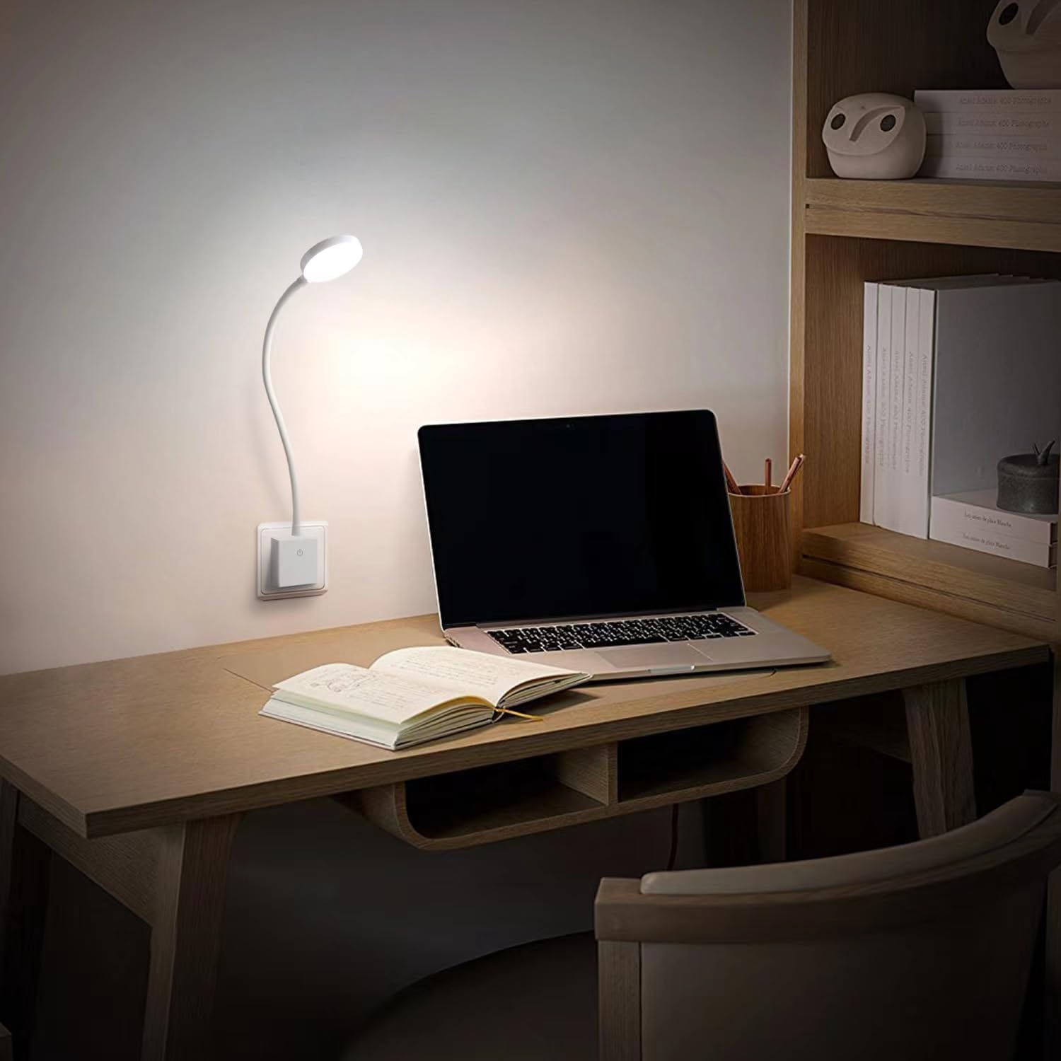 Laptop on a desk with an open book and a lamp in a dimly lit room