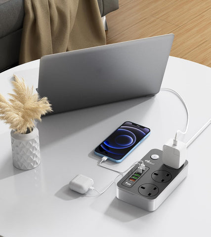 Laptop, smartphone, and power strip on a white table with a blurred background