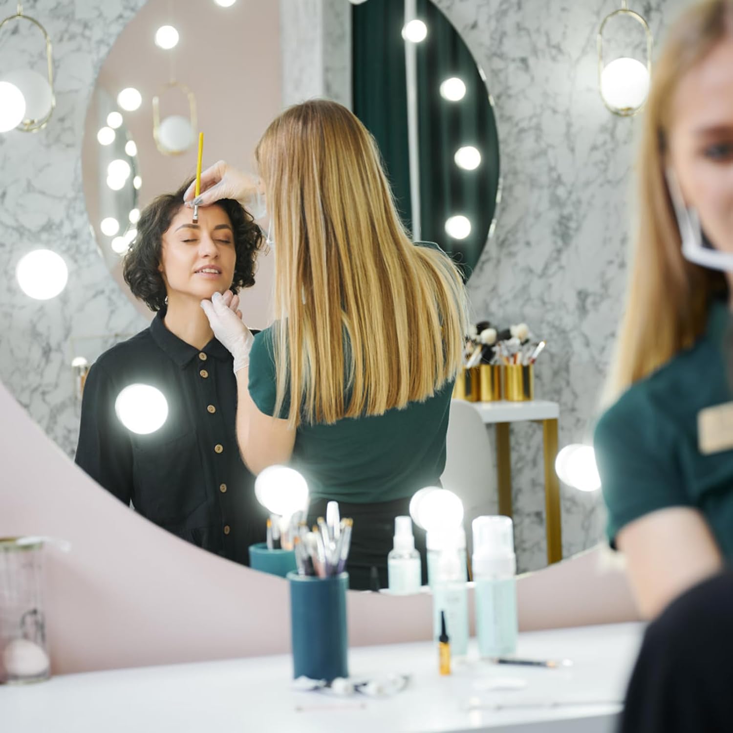Makeup artist applying makeup to a client in a salon setting with mirrors and products.