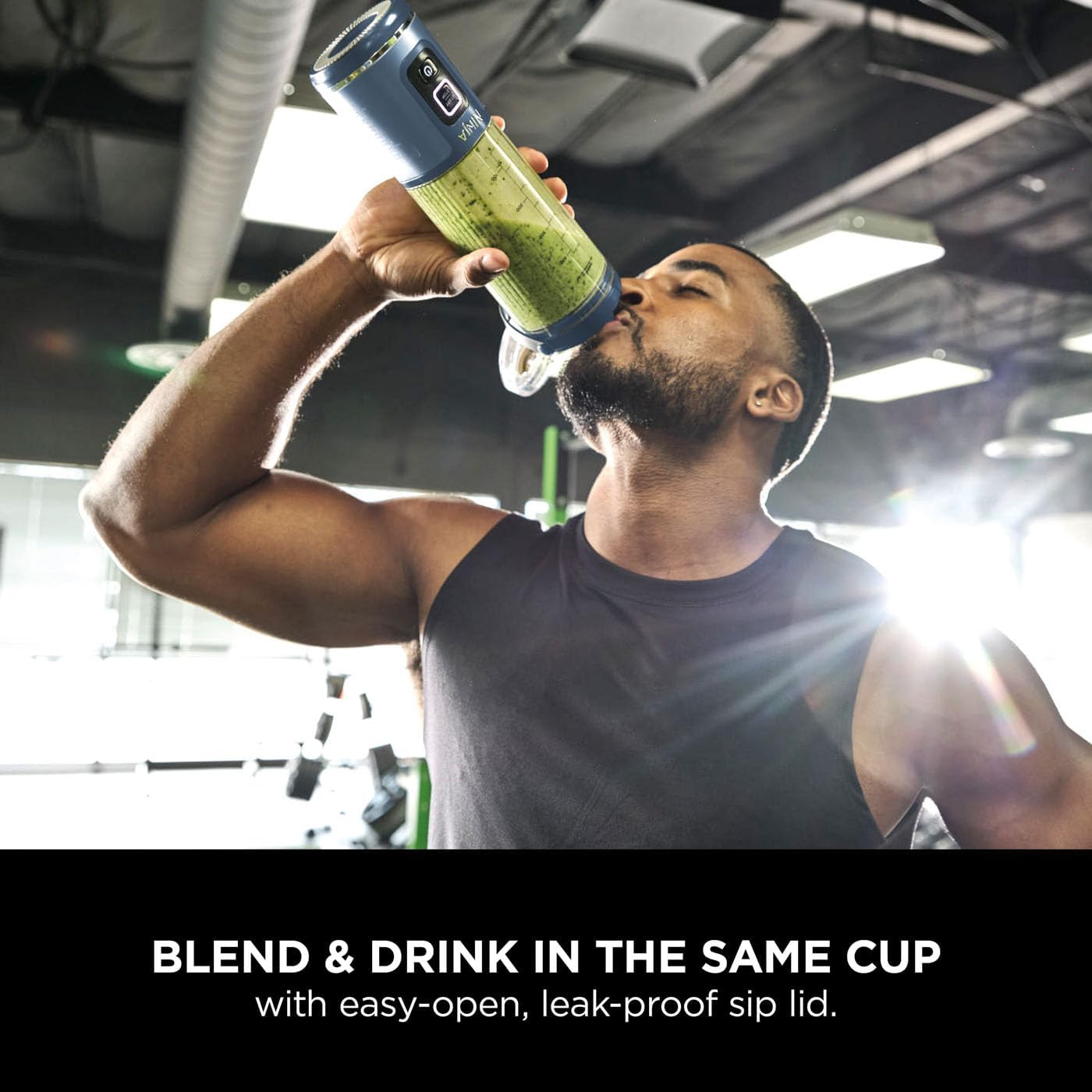 Man drinking from a green and blue shaker cup in a gym setting