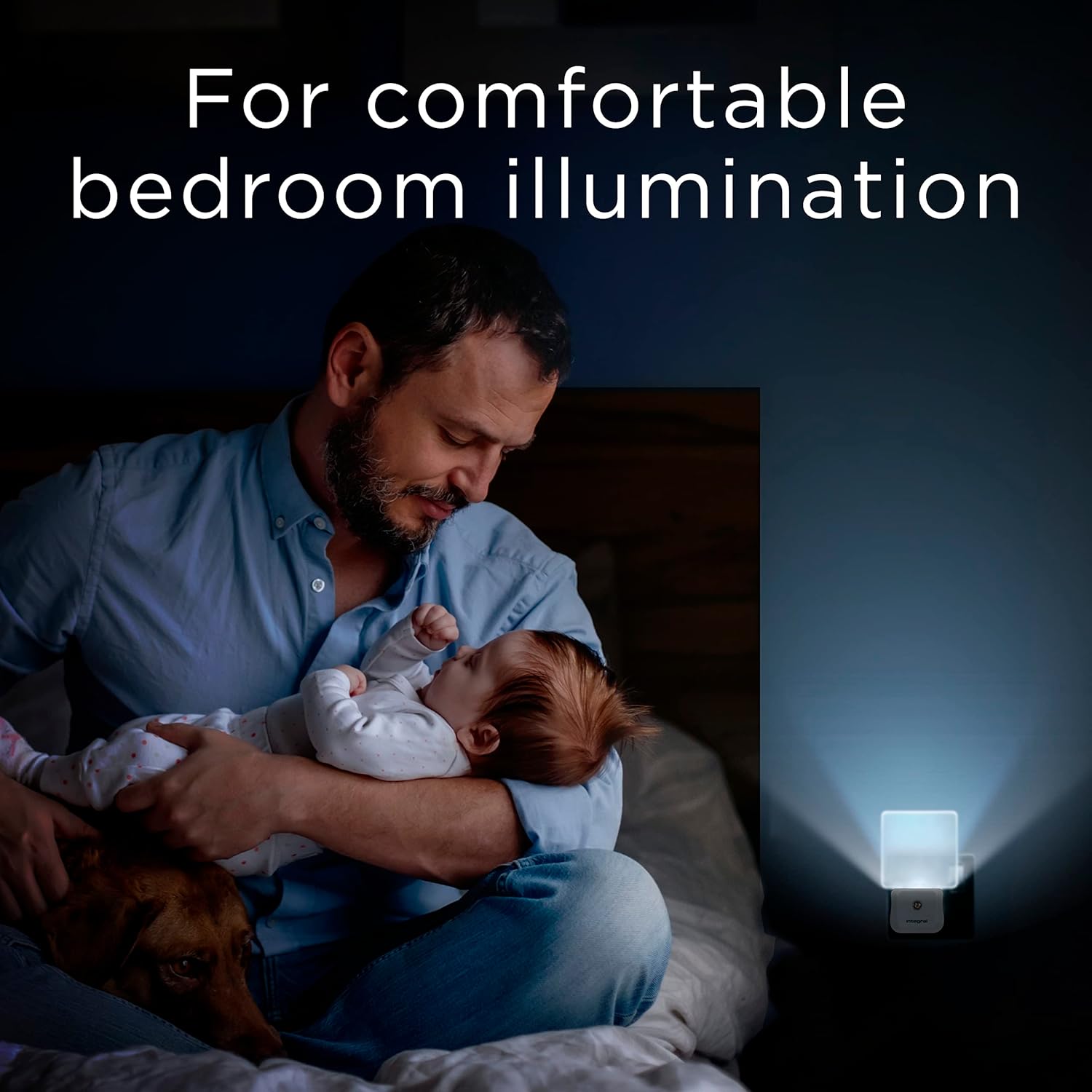Man holding a baby in a bedroom with a night light on the wall.
