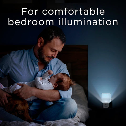 Man holding a baby in a bedroom with a night light on the wall.