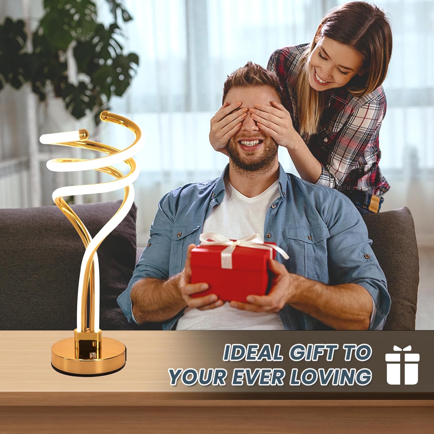 Man receiving a gift with a woman covering his eyes, gold lamp and red gift box on a table.