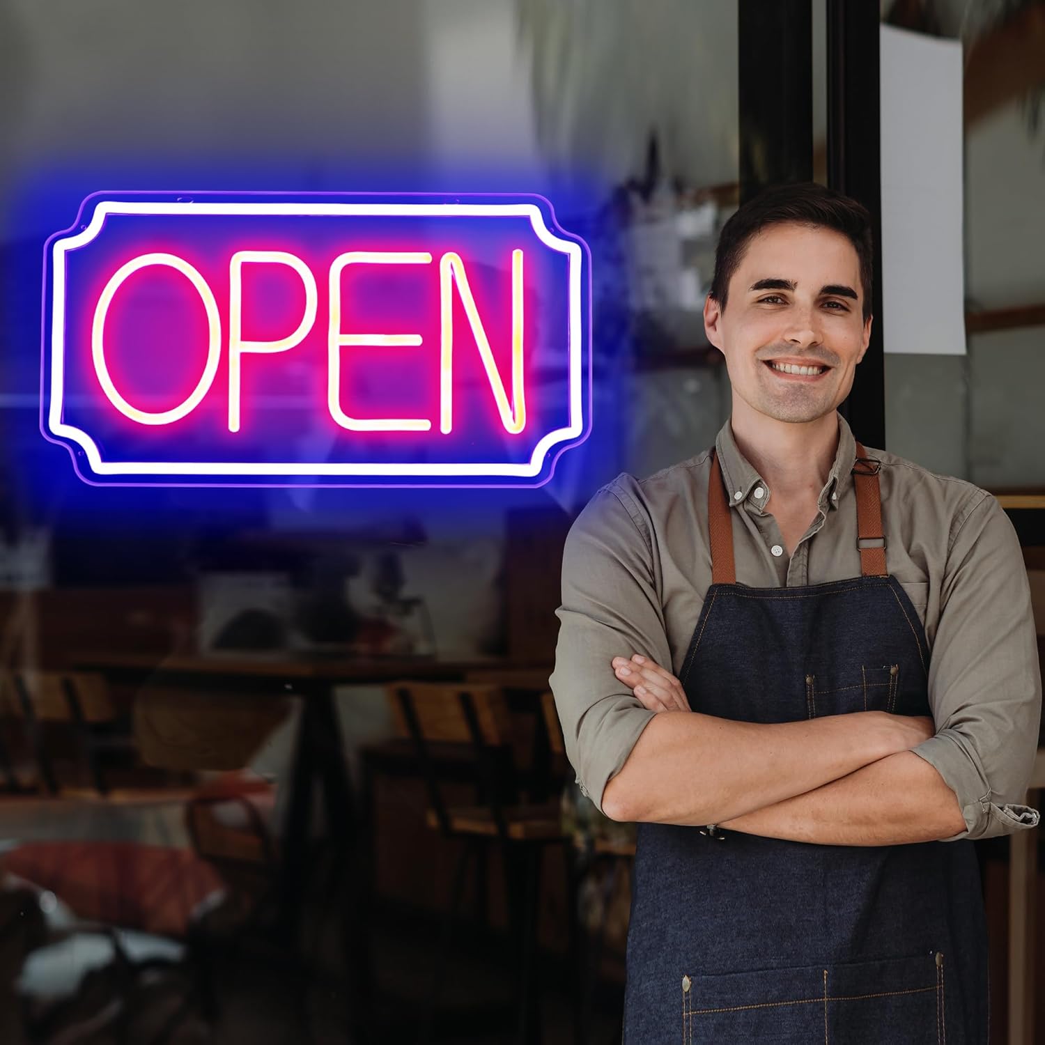 Man wearing an apron standing in front of a neon 'OPEN' sign inside a restaurant.