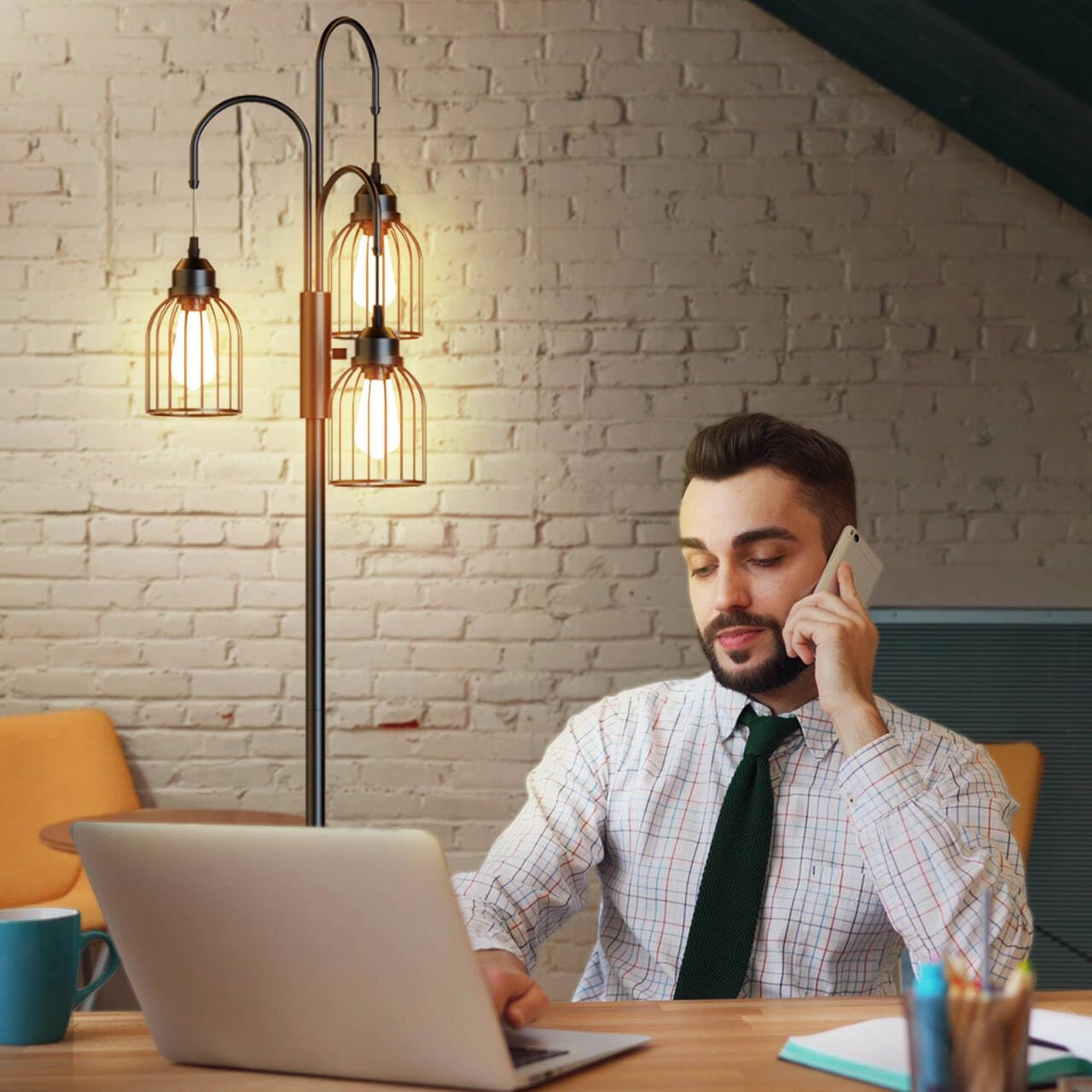 Man working at a desk with a laptop and phone, standing lamp in the background.