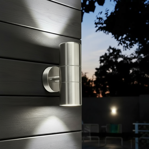 Metallic outdoor wall light fixture on a wooden surface with a night-time background.