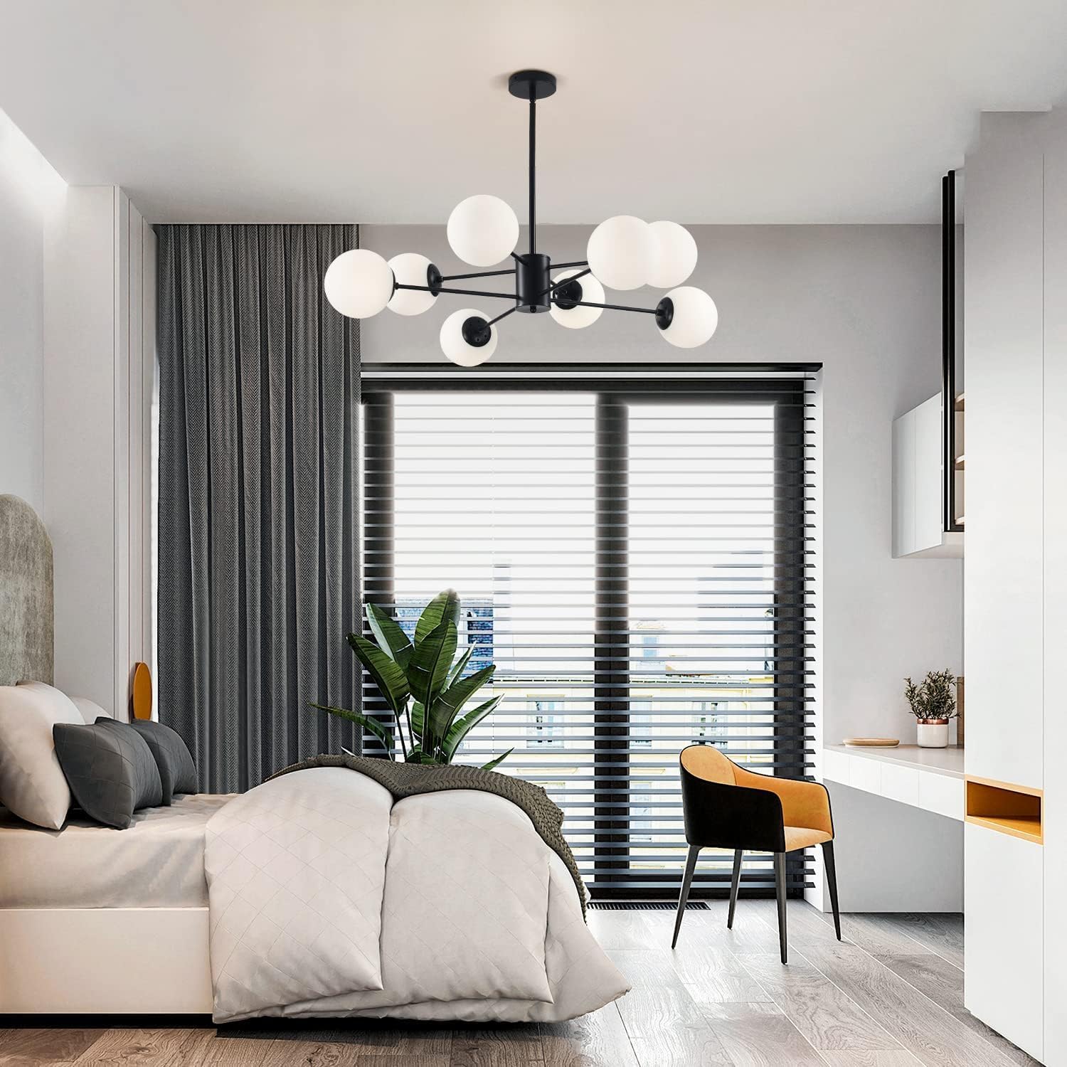 Modern bedroom with a chandelier, bed, desk, and plant.