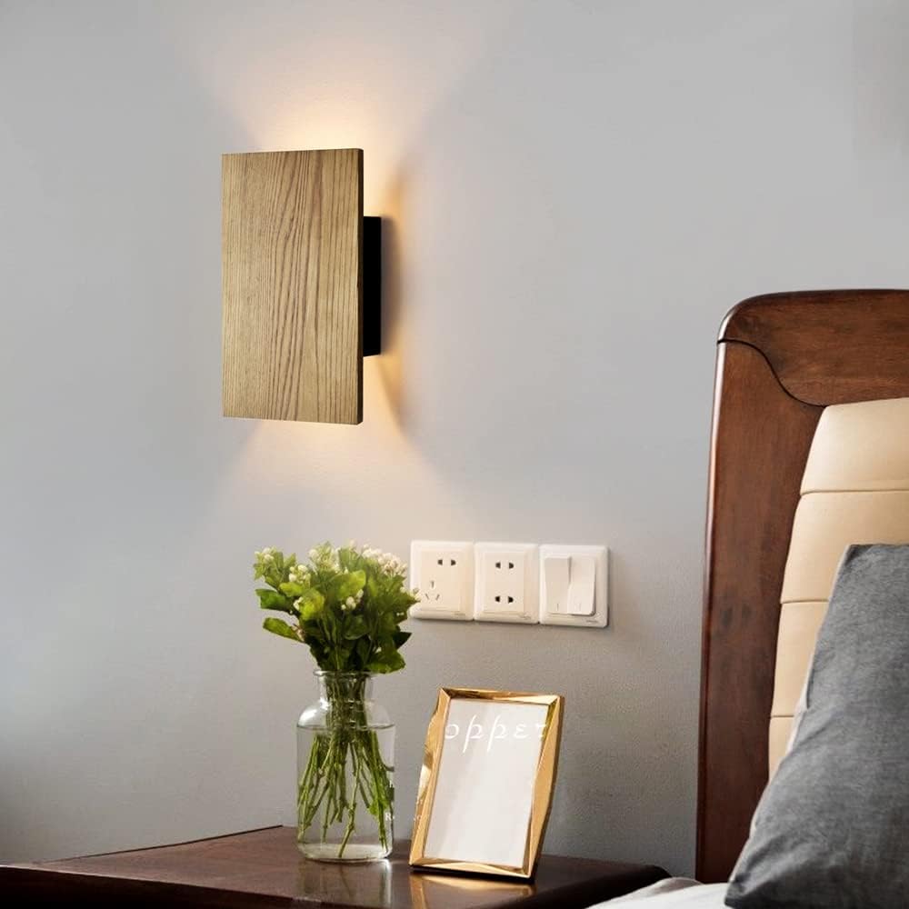 Modern bedroom with wall-mounted light fixture, vase with flowers, and framed picture.