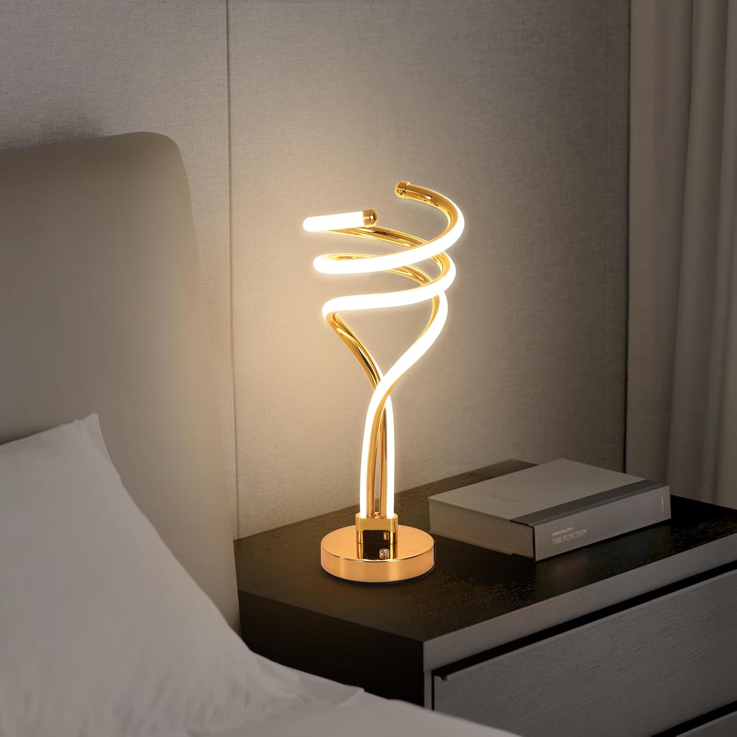 Modern gold spiral table lamp on a bedside table with a soft background