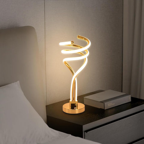 Modern gold spiral table lamp on a bedside table with a soft background