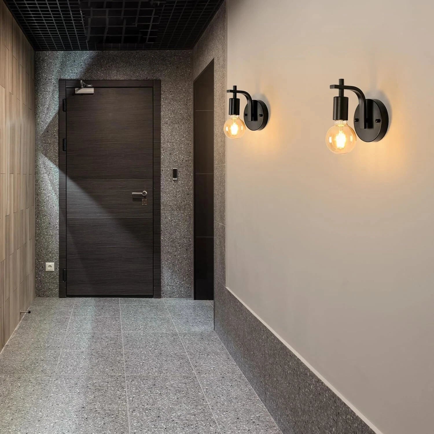 Modern hallway with a dark door, wall lights, and tiled floor.
