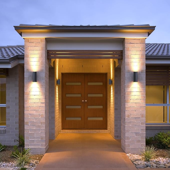 Modern house entrance with a wooden door and stone columns illuminated by lights.
