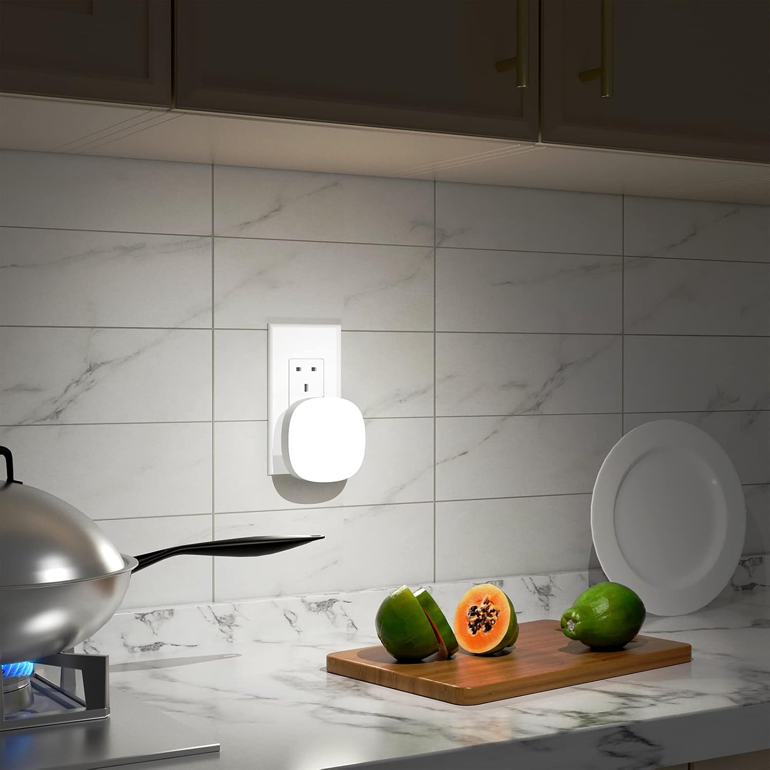 Modern kitchen with a wall-mounted light fixture, cutting board with fruits, and stove.